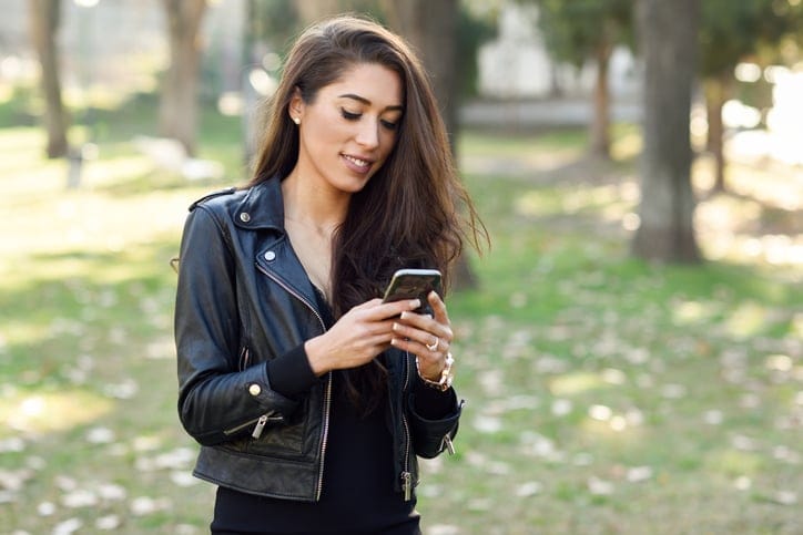 Young woman using a smartphone in an urban park. Girl wearing leather jacket.