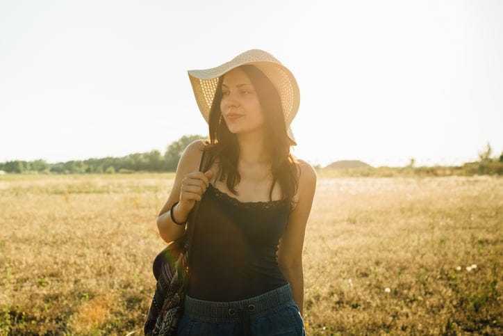 Fashionable girl walking in nature wearing hat, enjoying summer