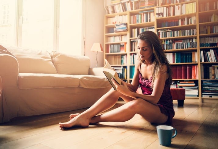 Woman dressed in a sexy lingerie reading a book and drinking her morning coffee.