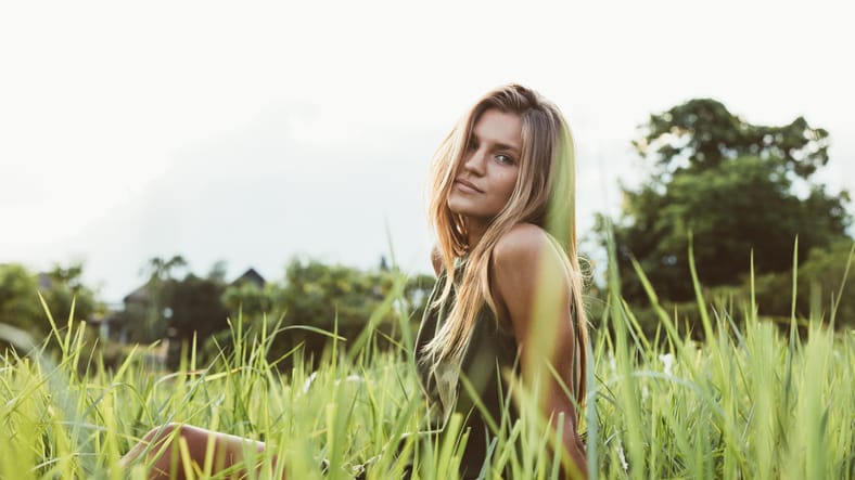 Portrait of cute young female model sitting in the meadow. Caucasian young woman outdoors in the field and looking at camera.