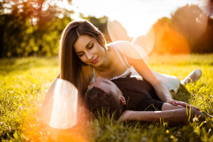 Young mixed race couple hugging in nature on grass - woman lies on man