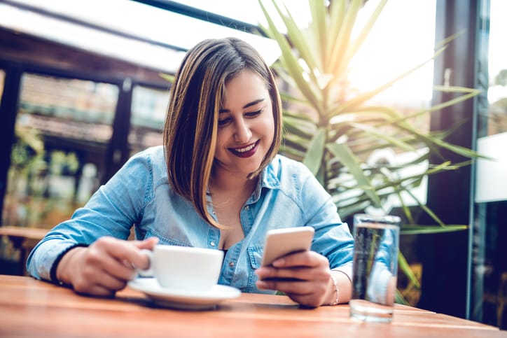 Young beautiful female using smartphone and drinking coffee at her favorite cafe place. Taking a break to connect.