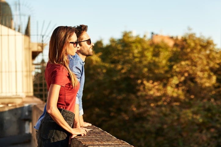 Shot of a smiling young couple leaning on a balcony in the city looking at the view