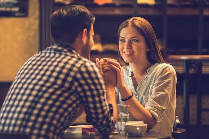 Affectionate couple looking at each other while holding hands in a cafe. Focus is on young woman.
