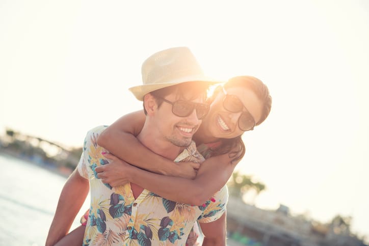 Attractive Couple smiling with Piggyback Ride at the beach, they are heaving fun and spending time together on romantic getaway.