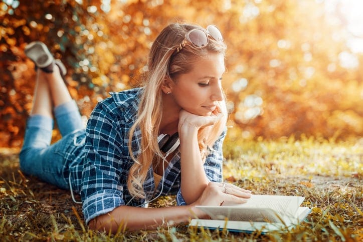 Portrait of a gorgeous young woman reading a book in the autumn park.