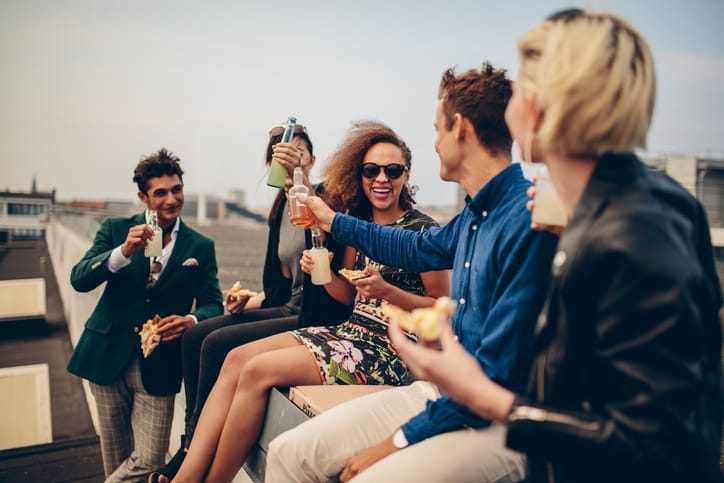 Multiethnic group of young friends partying on terrace, drinking and celebrating. Young men and women having drinks on rooftop.