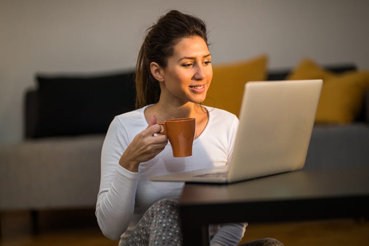 Woman sitting on the floor in the morning drinking coffee and using laptop
