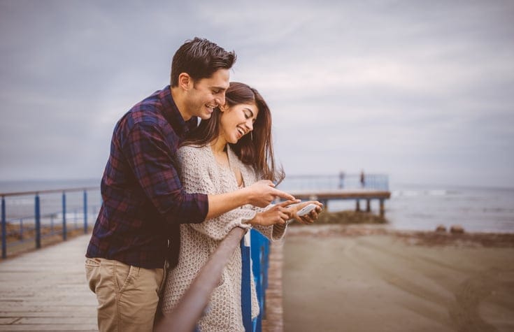 Adorable mediterranean couple looking at photo on mobile phone, smiling together