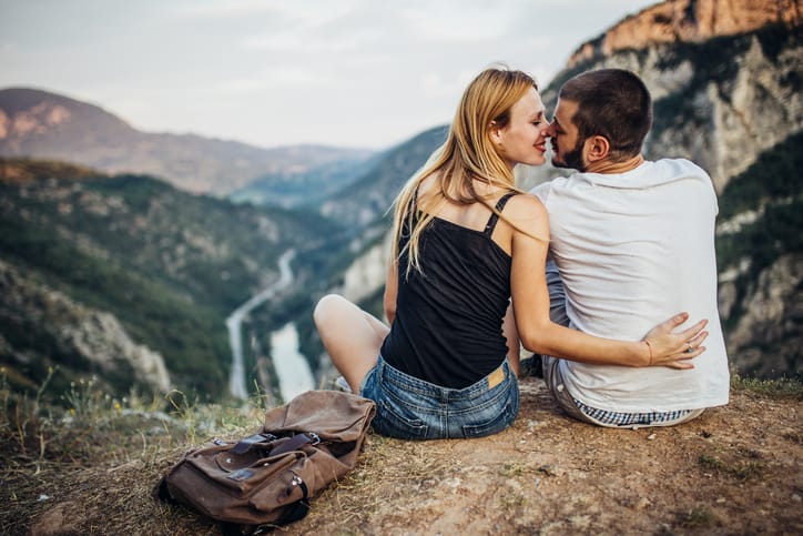 Two people, man and woman, heterosexual couple, sitting on mountain, rear view, kissing on motuh.