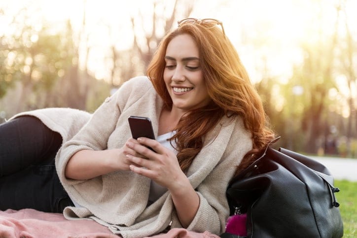 young woman happy texting park sun