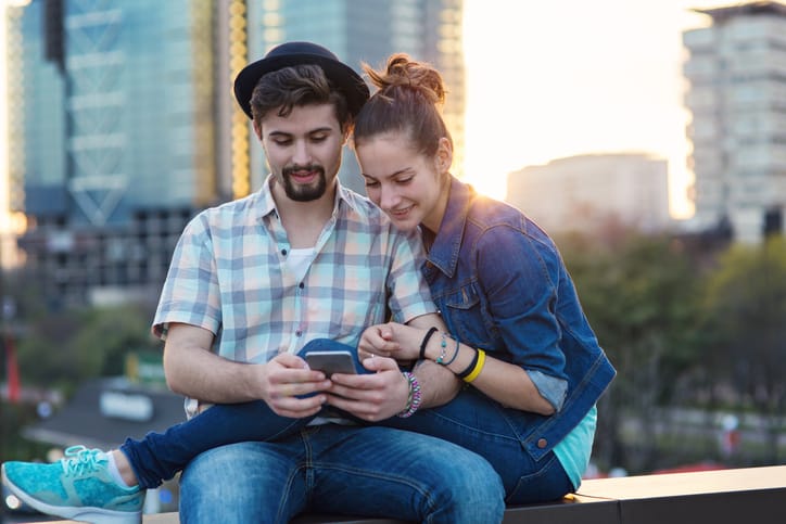 Couple sitting on a bridge parapet and browsing together on a mobile phone