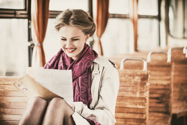 Retro styled portrait of a beautiful young woman sitting in a vintage train wagon, reading good news in a letter.