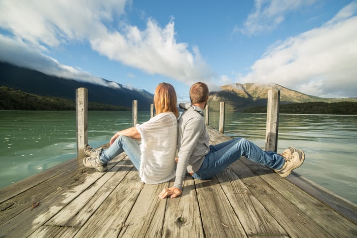 Couple sits back to back on lake pier