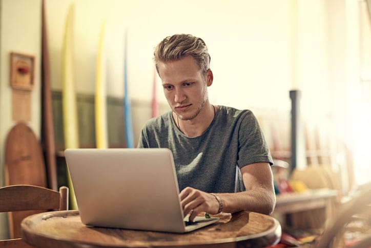 Shot of a happy young man using his laptop while relaxing at home