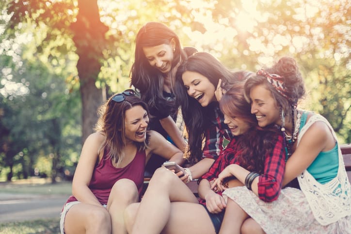 Happy girls in the park texting on smartphone