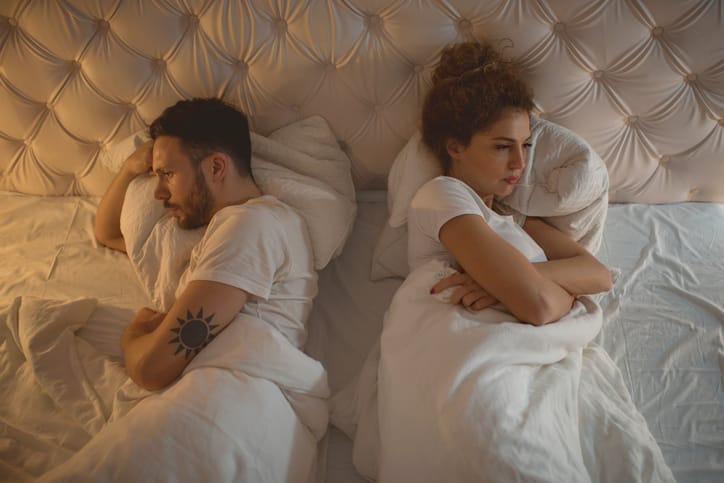 High angle view of young couple lying back to back in bed while being angry at each other.