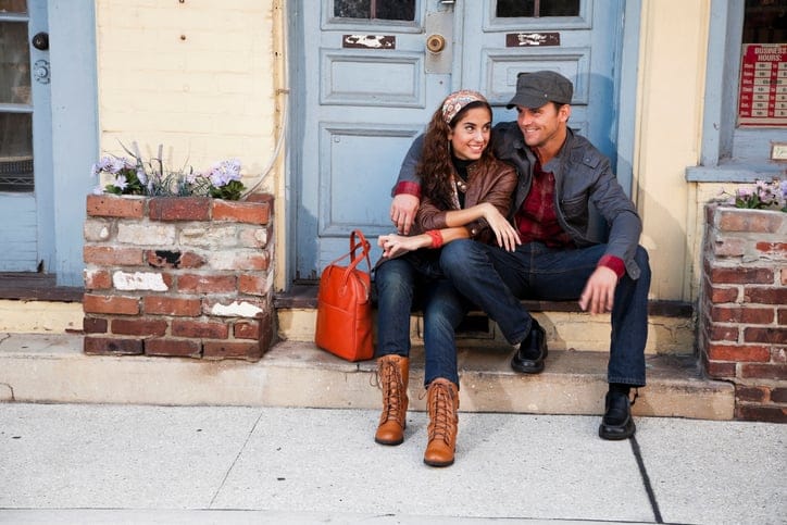 Young affectionate couple sitting on doorstep outside small town shop.
