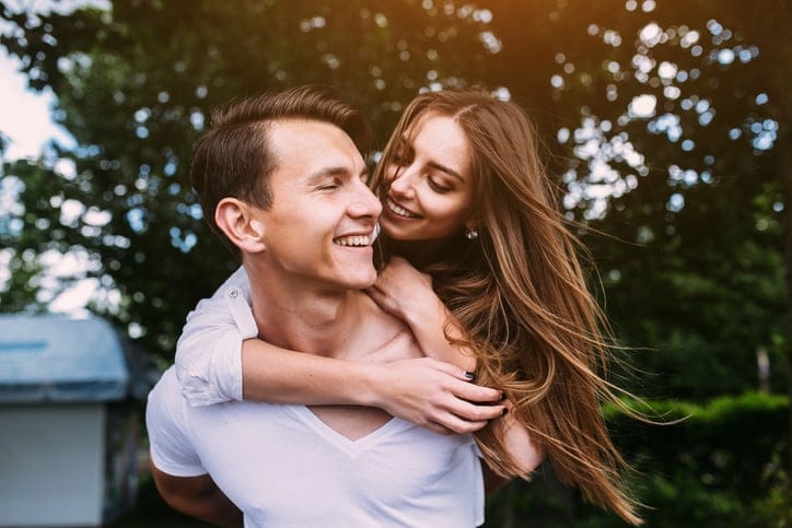 Young man carries his girlfriend on his back in the park