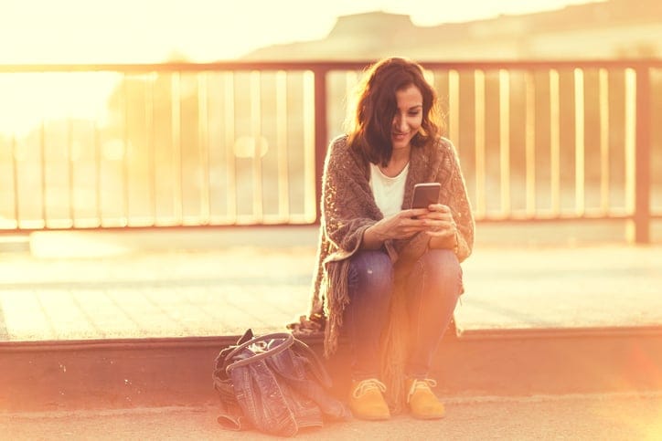 Young woman sitting outdoors,using phone and smiling
