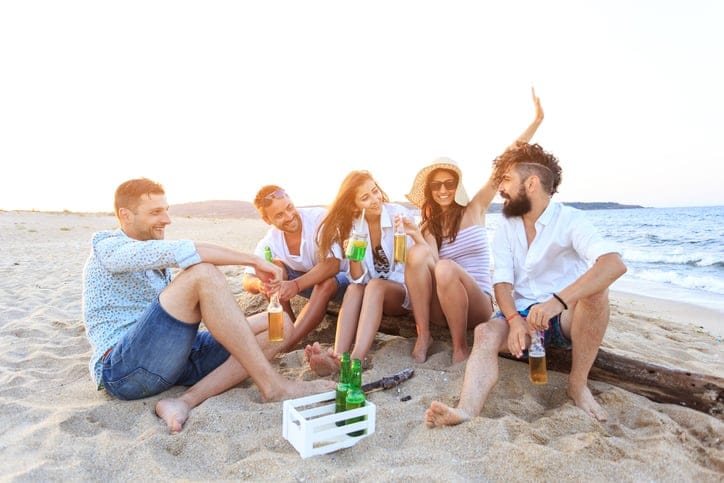 Friends sitting on sand and drinking beer.