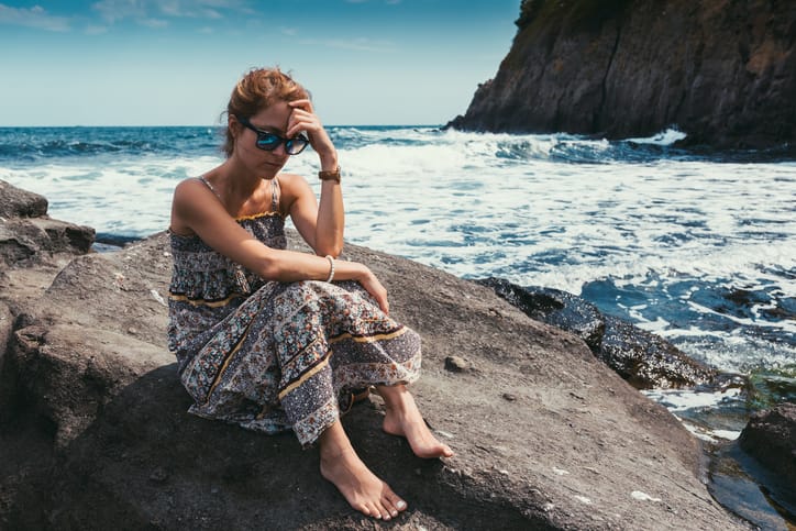 Unhappy woman sitting thoughtfully at the rocks