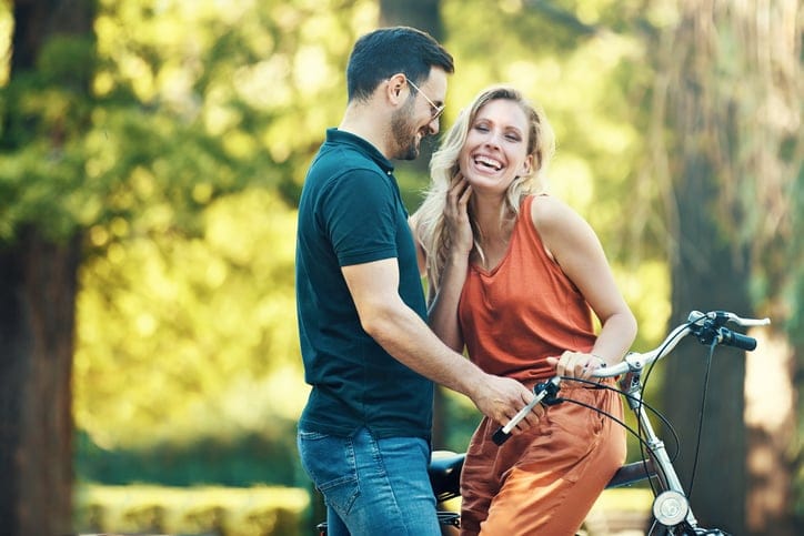 Portrait of happy young couple riding a bike in the park.