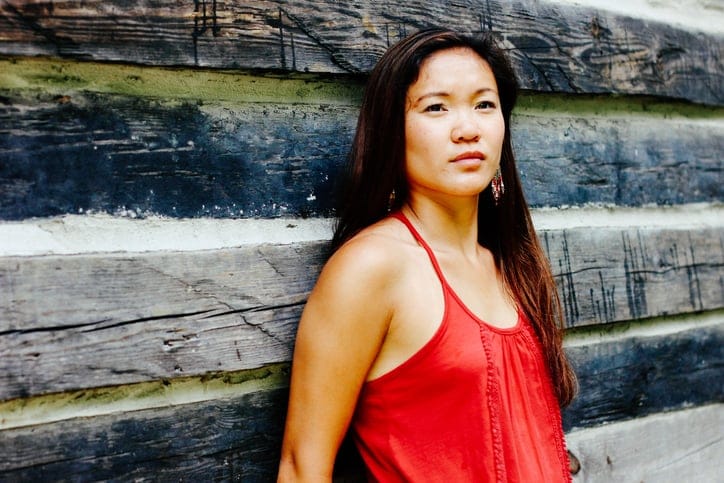 An Asian woman against a wood wall.