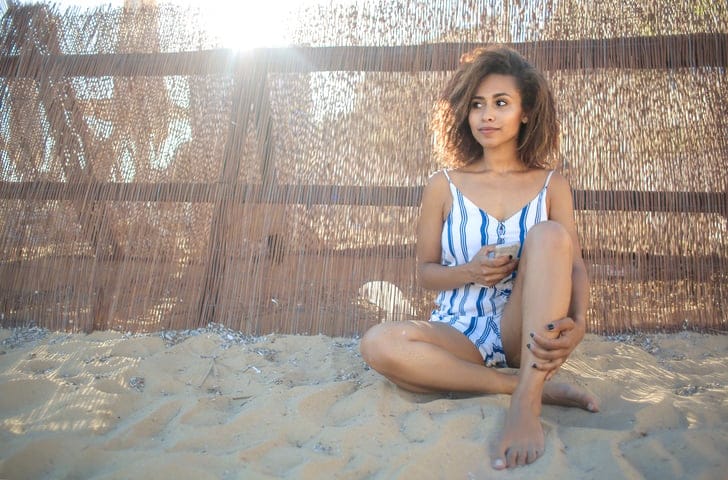 Girl sitting at the beach, holding a smart phone
