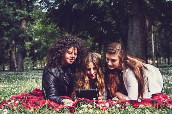3 beautiful woman look in tablet computer in park on grass