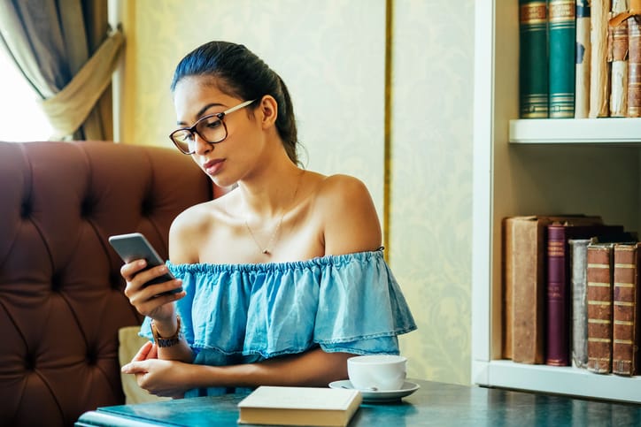 young woman using her smart phone ,coffee and book on the table