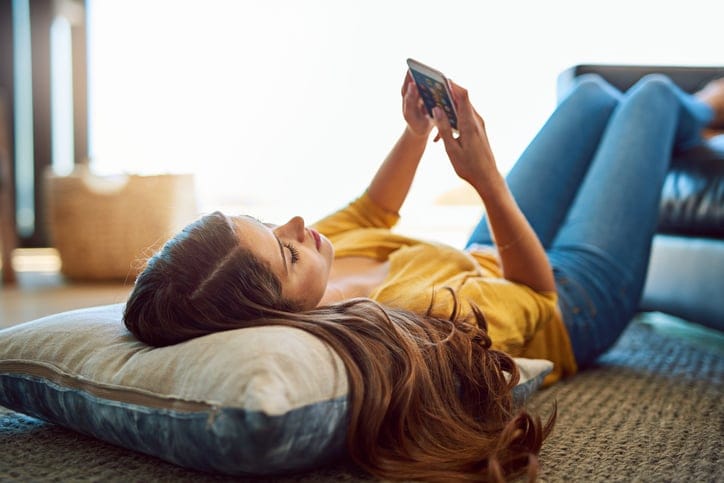 Shot of a young relaxing on the floor and using a smartphone at home