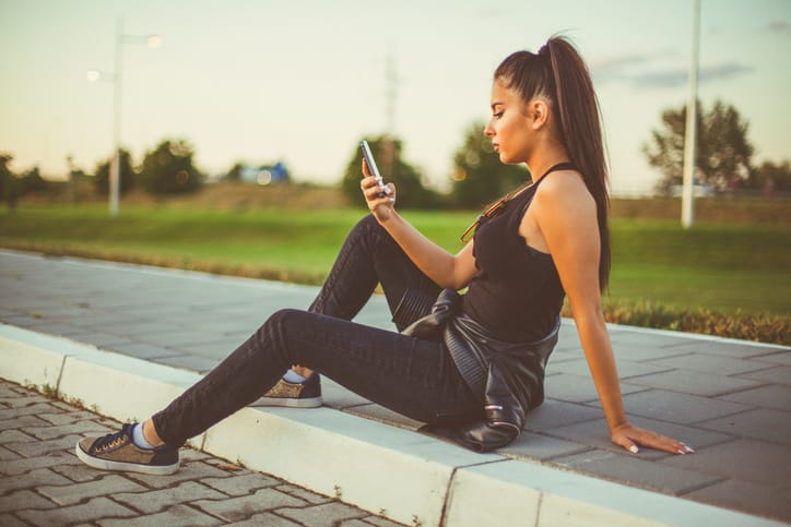 Beautiful woman sitting and texting at the street road
