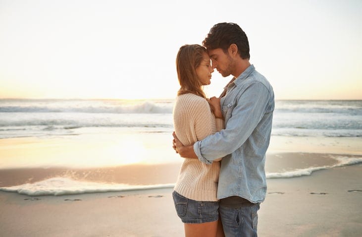 Side view of a blissful young couple embracing on the beach at sunset