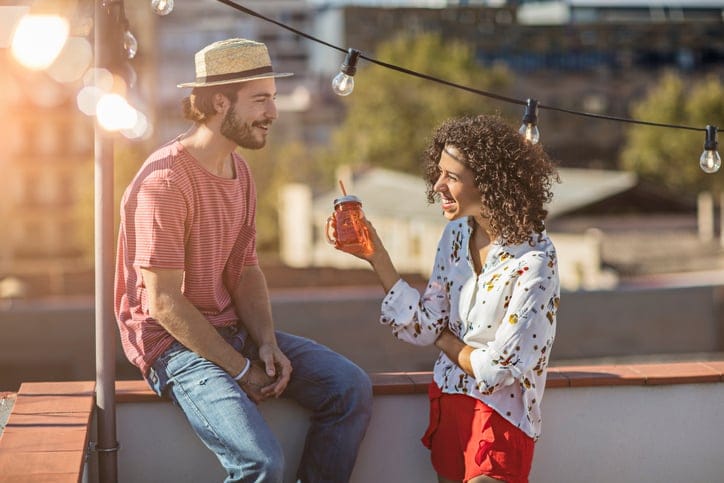 Outdoor shot of young couple with drinks talking on a rooftop party