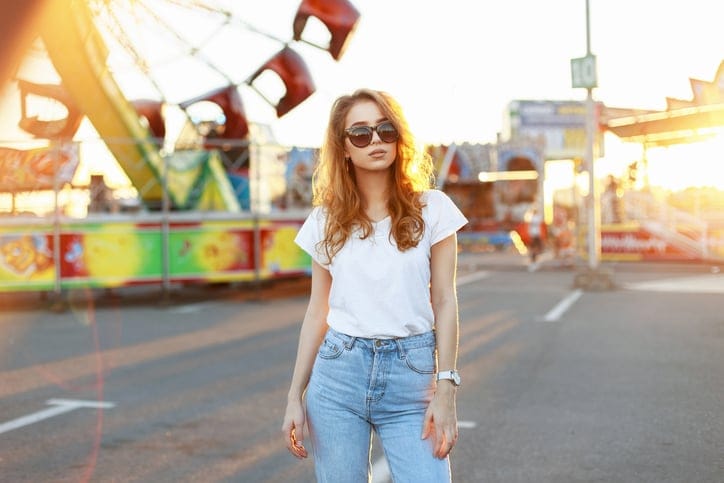 Beautiful young stylish woman in sunglasses walking in the amusement park at sunset.