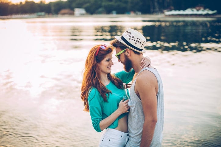 Young couple walking on the beach. Wearing boho style clothing and drinking beer. Enjoying in sunset.
