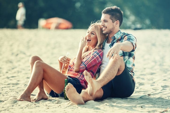 Young couple enjoying free time on the beach and drinking beer.