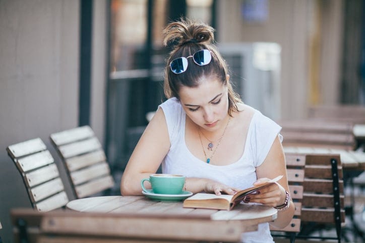Girl Drinking Coffee and Reading Book in Cafe