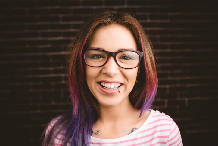 Portrait of smiling woman in spectacles against brick wall