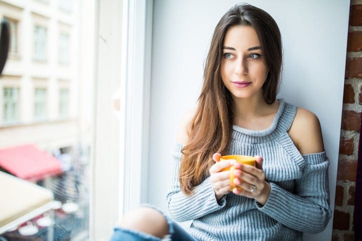 young girl enjoying an ideal day sitting in the window-sill. Wearing casual denim jeans and blouse, crossing legs
