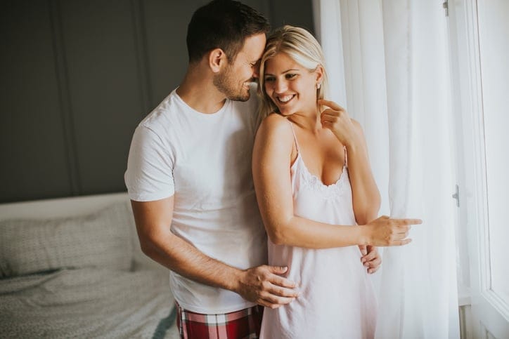 Lovely young couple standing by the window at morning in bedroom
