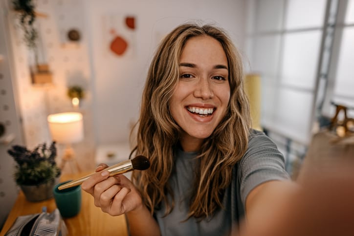 Woman applying makeup while taking a selfie.