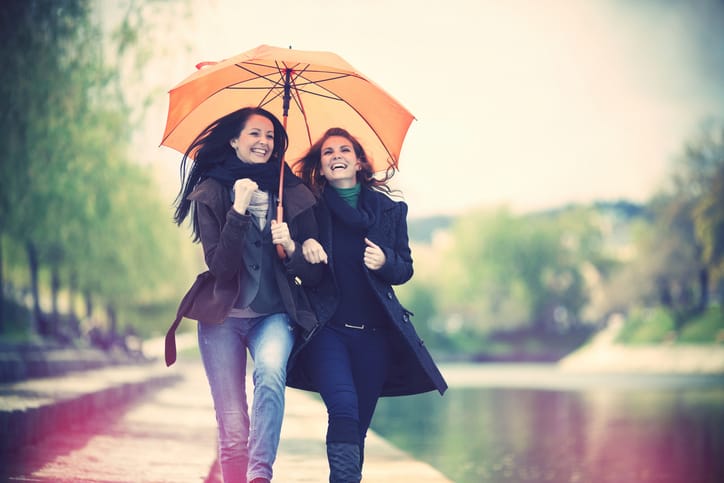 Two girl friends laughing, arms around each other and walking