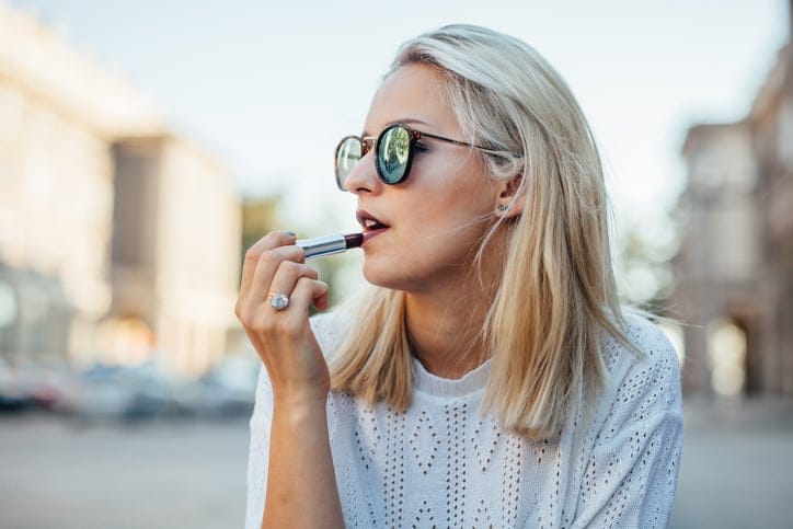 Young fashionable woman is sitting and painting lips. Urban background