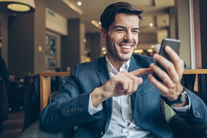 Smiling businessman with smart phone sitting in cafe.