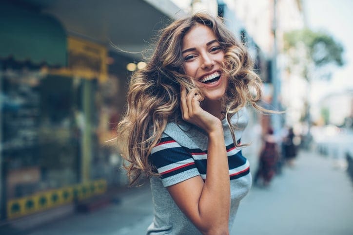 Smiling young woman with smart phone walking on the street and turning to look back, with copy space.