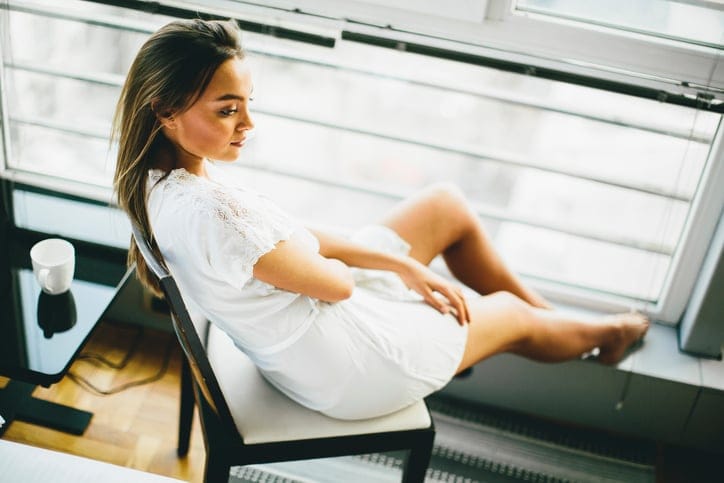 Young woman sitting and dreaming on a chair by the window in her nightgown