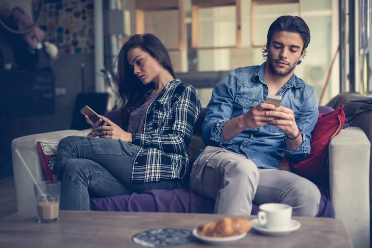 Young couple sitting in a cafe and each of them is using their own mobile phone. Focus is on man.