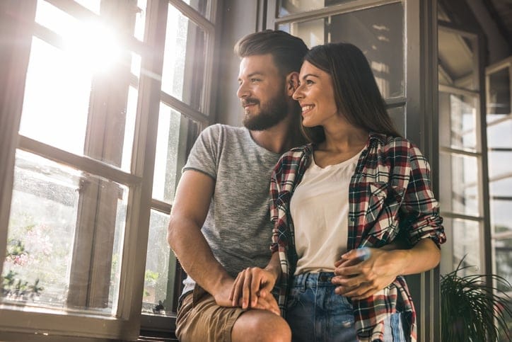 Happy couple in love looking through the window at their apartment.